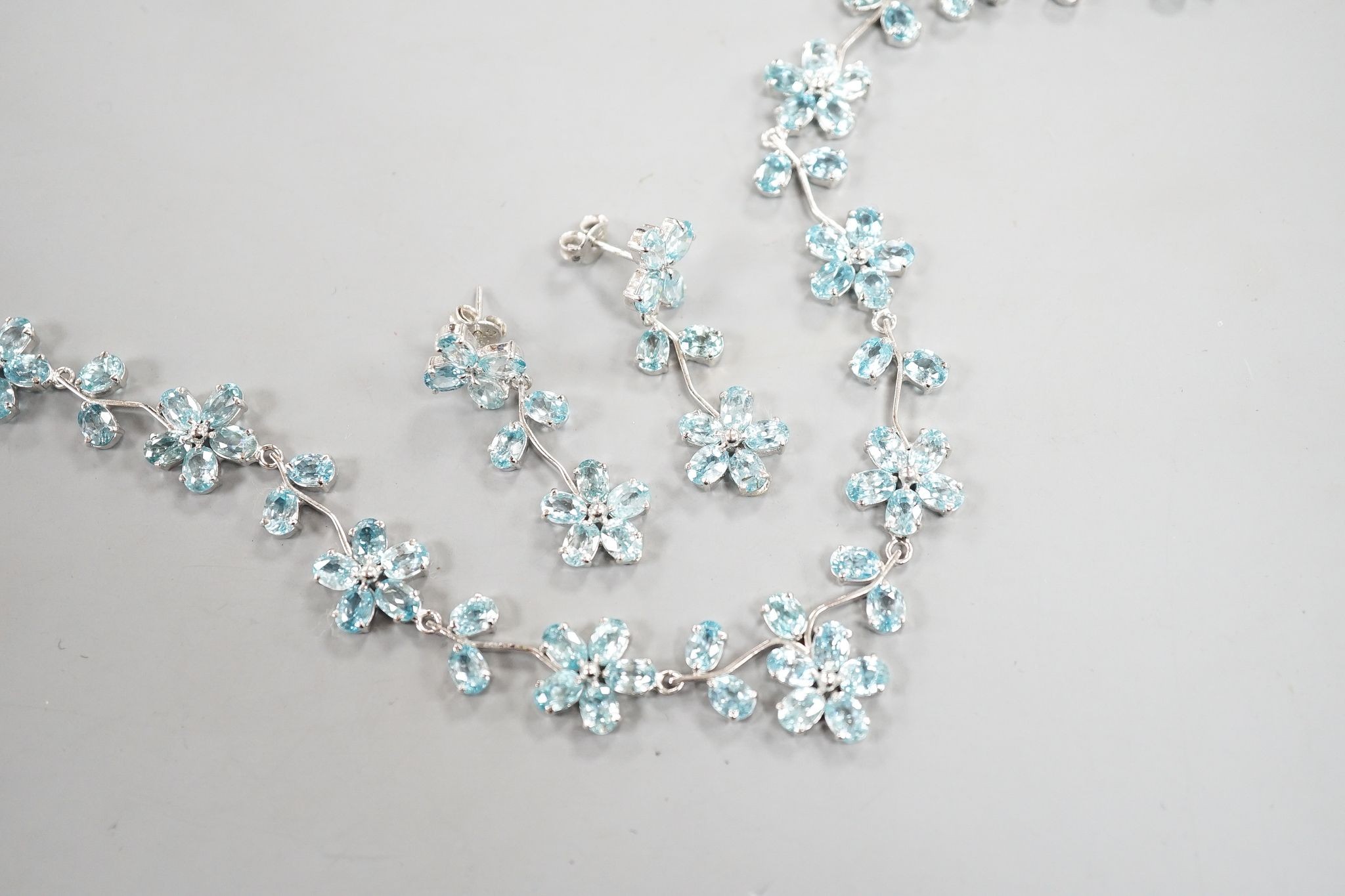 A modern 925 and blue zircon suite of jewellery, comprising a flower head cluster necklace and a pair of matching earrings.